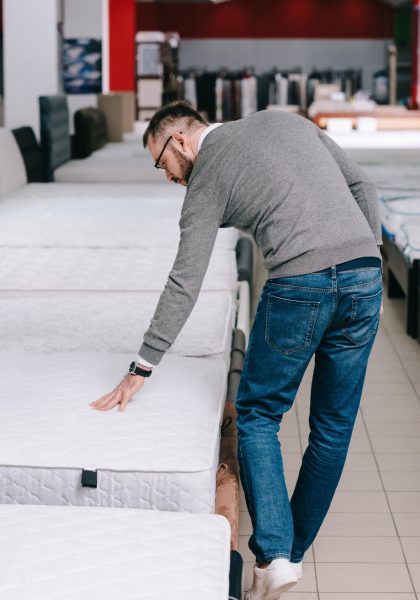 back view of man choosing mattress in furniture store
